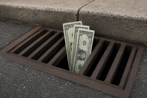 Dollar bills going down the a storm drain