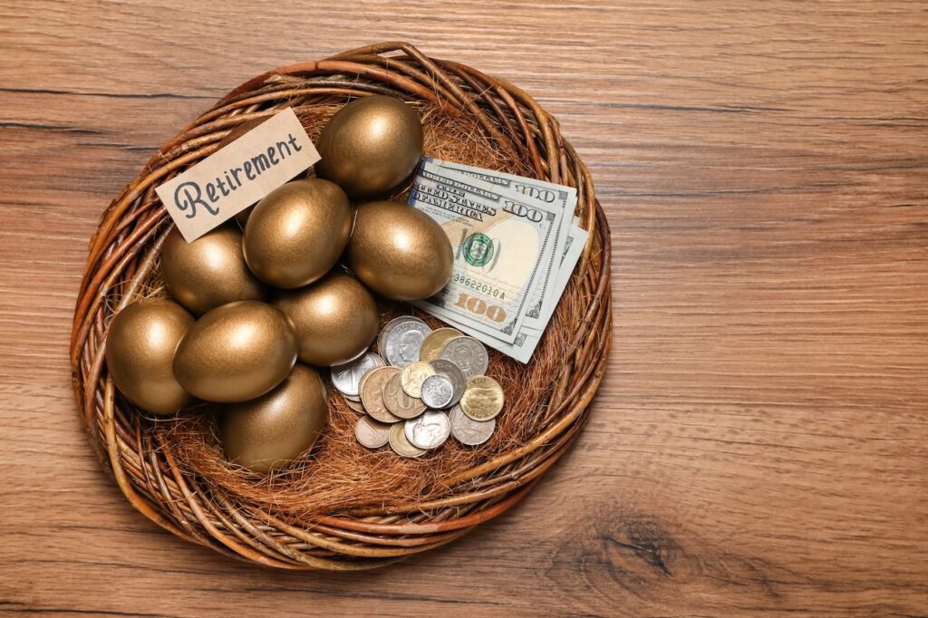 Golden eggs, money and card with word Retirement in nest on wooden table, top view. Pension concept